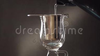 用金属过滤器在玻璃杯中冲泡茶。 水壶里的热水通过钢水过滤器流入玻璃